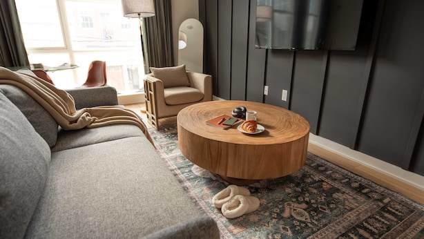 Una sala de estar moderna con un sofá gris, una mesa de centro redonda de madera y una alfombra estampada.