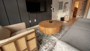 Una sala de estar moderna con un sofá gris, un sillón de mimbre, una mesa de centro redonda de madera y una alfombra estampada.