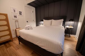 A neatly made bed with white linens, a bedside table with a lamp, and a wooden side table with a towel. - Sosuite 2BR Apt w Patio W D Sofabed (Philadelphia)