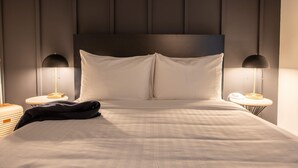 Ein ordentlich bezogenes Bett mit weißen Laken, zwei Nachttischlampen und ein runder Nachttisch mit Telefon und Lampe.