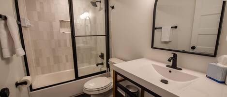 Une salle de bain moderne avec une douche à parois de verre, des toilettes blanches, un lavabo avec un miroir et un porte-serviettes.