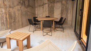 Ein kleiner, abgeschlossener Patio-Bereich mit einem runden Holztisch und vier Stühlen, einer Holzbank und einer Glastür.