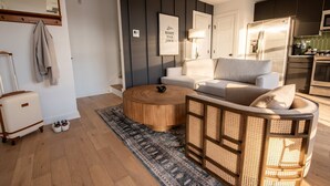 Uma sala de estar moderna com sofá, mesa de centro e uma cadeira de vime. Uma mala e sapatos estão no chão.