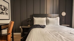 Quarto de hotel bem arrumado, com uma cama grande, uma escrivaninha e uma cadeira.