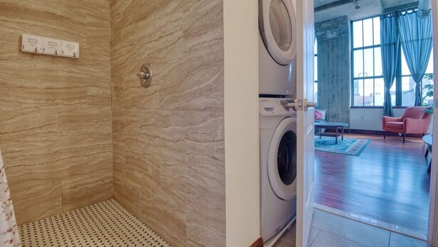 A bathroom with a shower, a washing machine, and a view of a living room with a chair and a table. - Sosuite 2BR Apt w W/d, Gym, On-site Restaurant (Philadelphia)