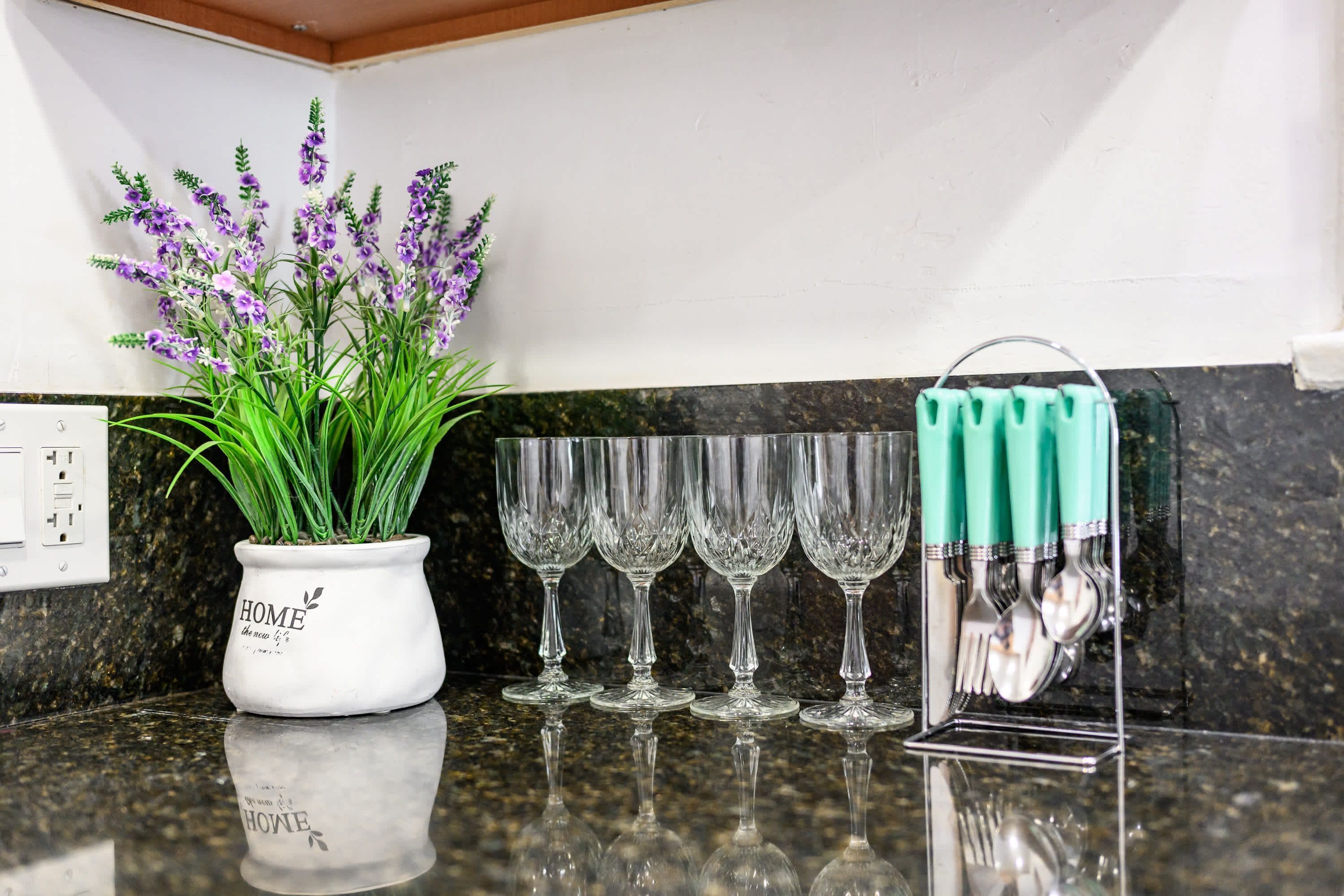 Una encimera de cocina con una maceta de lavanda, cuatro copas de vino y un portalapices con mangos verdes.