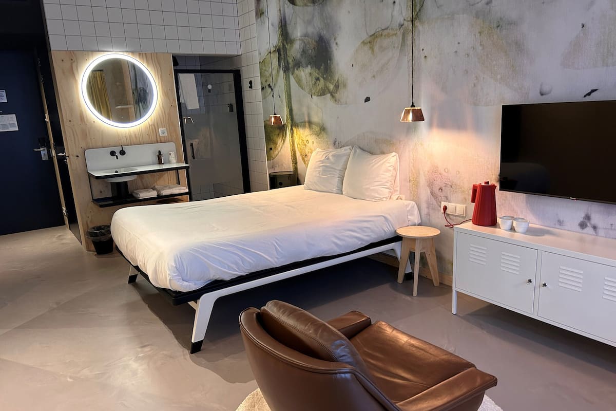 Une chambre à coucher moderne avec un lit, un miroir rond, une table de chevet, un téléviseur et un fauteuil en cuir.