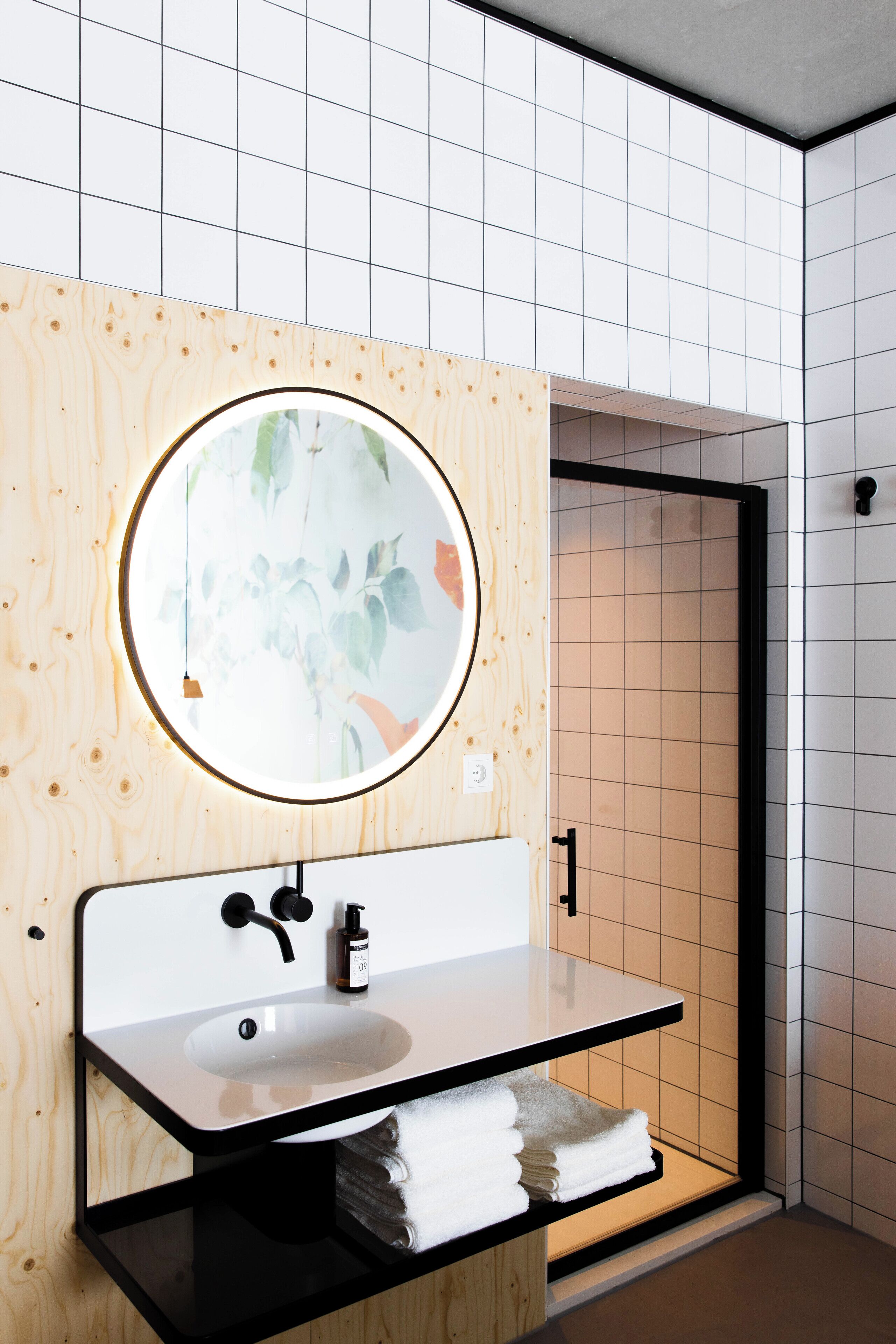 A modern bathroom with a wooden vanity, a round mirror, and a white sink.