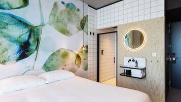 Una habitación de hotel moderna con una cama grande, un espejo redondo fijado a la pared y un panel de madera con lavabo integrado.