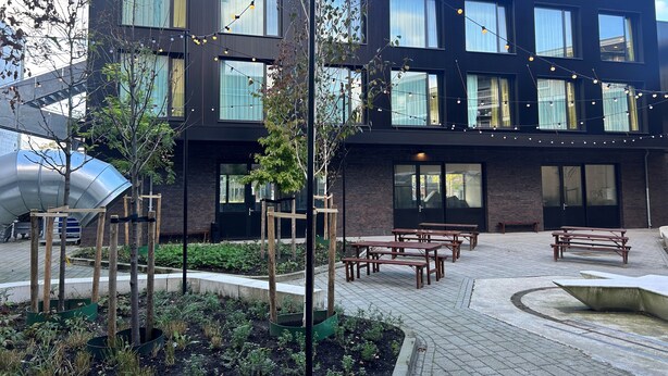 Un edificio moderno con muchas ventanas, mesas al aire libre y luces colgantes.