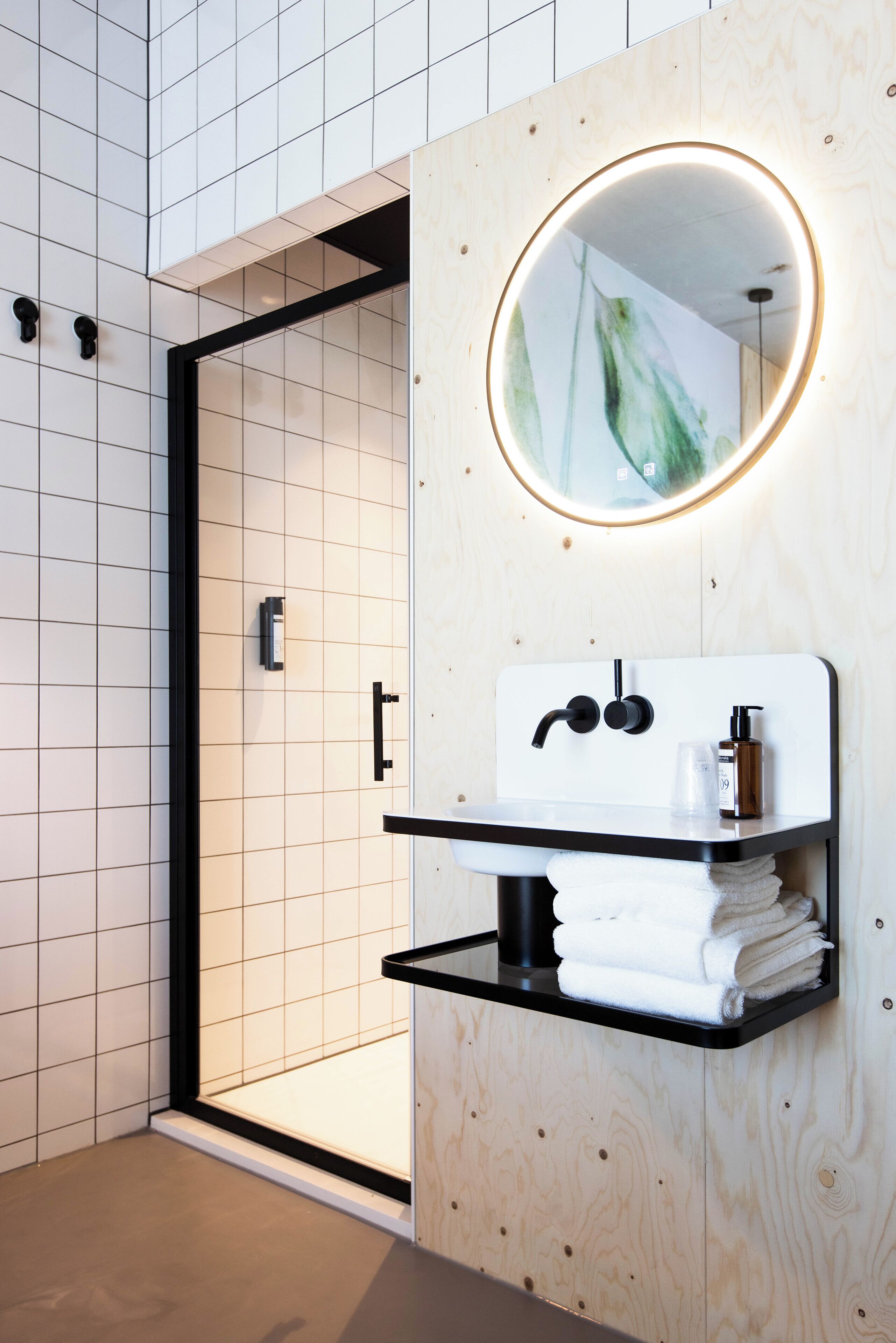 A modern bathroom with a wooden vanity, a round mirror, and a glass shower enclosure.
