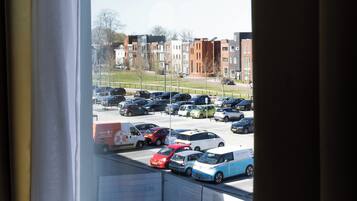 Vista a través de una ventana que muestra un estacionamiento con varios coches, una obra en construcción y edificios residenciales al fondo.