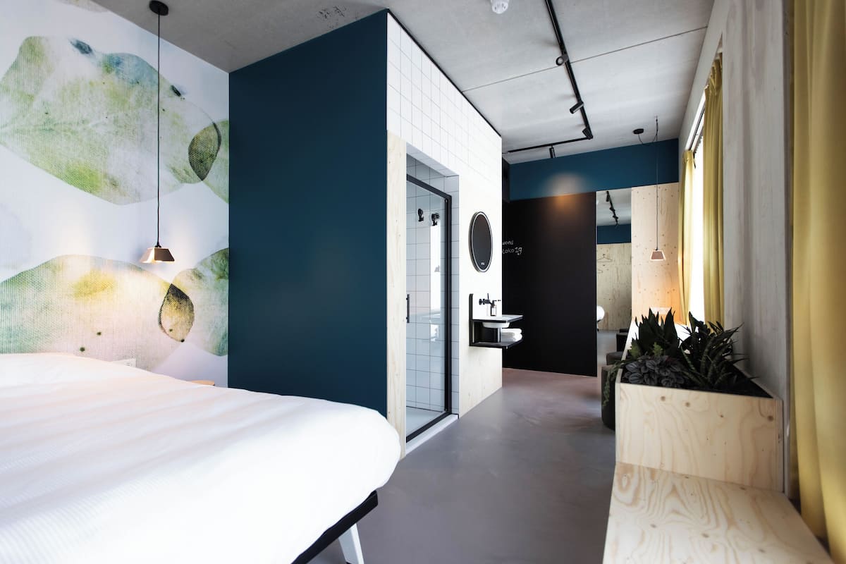 Une chambre d’hôtel moderne dotée d’un grand lit, d’une salle de bain avec une porte en verre et d’un petit coin salon agrémenté de plantes.