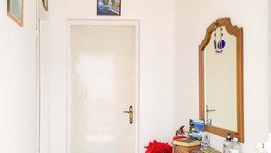 Un couloir avec une porte blanche, un meuble en bois doté d’un miroir et deux grands vases.