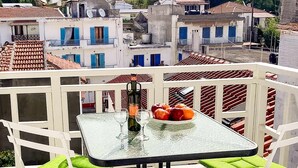 A glass table with two chairs on a balcony with a stone floor, overlooking a town with terracotta roofs. - Dinas Apartment - Alonnisos Summer Haven (Alonissos)