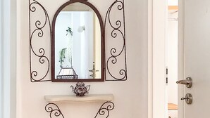 A hallway with a mirror, a small shelf with a decorative item, and a wicker basket. - Dinas Apartment - Alonnisos Summer Haven (Alonissos)