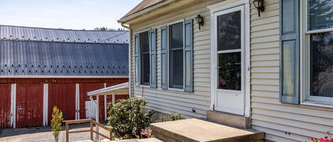 A house with a front porch, a small garden, and a red barn in the background.