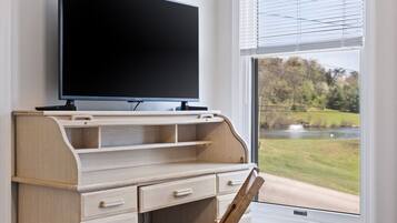 A bedroom with a wooden desk, a television, a chair, and a window with blinds.