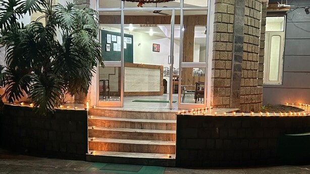 A building entrance with a staircase leading up to a door, surrounded by a brick wall and a large potted plant. - Gagan Resort (Dharamshala)