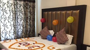A neatly made bed with a floral bedspread, pillows, and balloons. - Gagan Resort (Dharamshala)