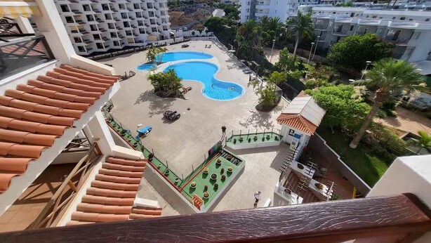 A rooftop pool area with multiple pools, surrounded by greenery and buildings. - San Marino 38 - One Bed (Arona)