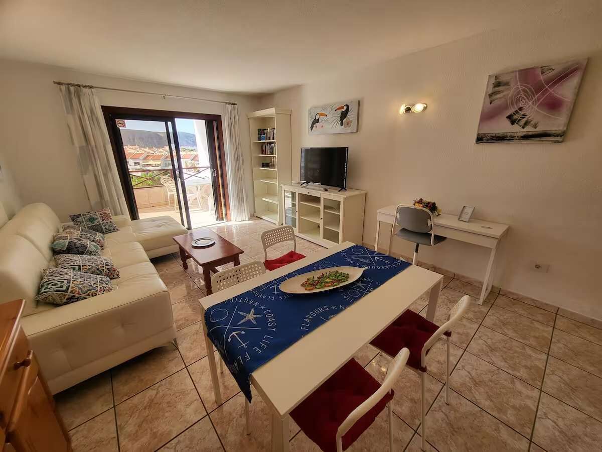 Un salon avec un canapé, une table à manger recouverte d’une nappe bleue, un téléviseur et une bibliothèque.