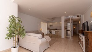 A modern living room with a sofa, a dining area, and a kitchen in the background. - Palms 4 - Three Bed S (Golf del Sur)