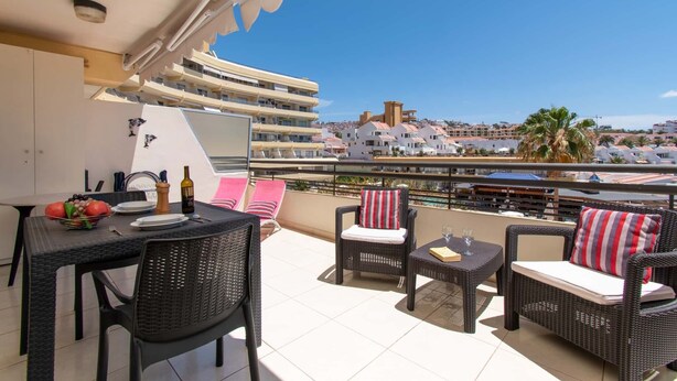 Un balcon aménagé avec du mobilier d’extérieur, une table à manger et une vue sur les bâtiments et les palmiers.