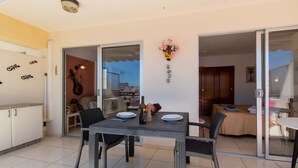Un coin repas avec une table dressée pour deux personnes, une guitare appuyée contre le mur et une porte-fenêtre coulissante donnant sur une chambre.