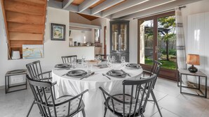 A dining area with a round table set for six, surrounded by six chairs. There is a window with a view of greenery outside. - House with an extension for 11 at 800m from the sea (La Plaine-sur-Mer)