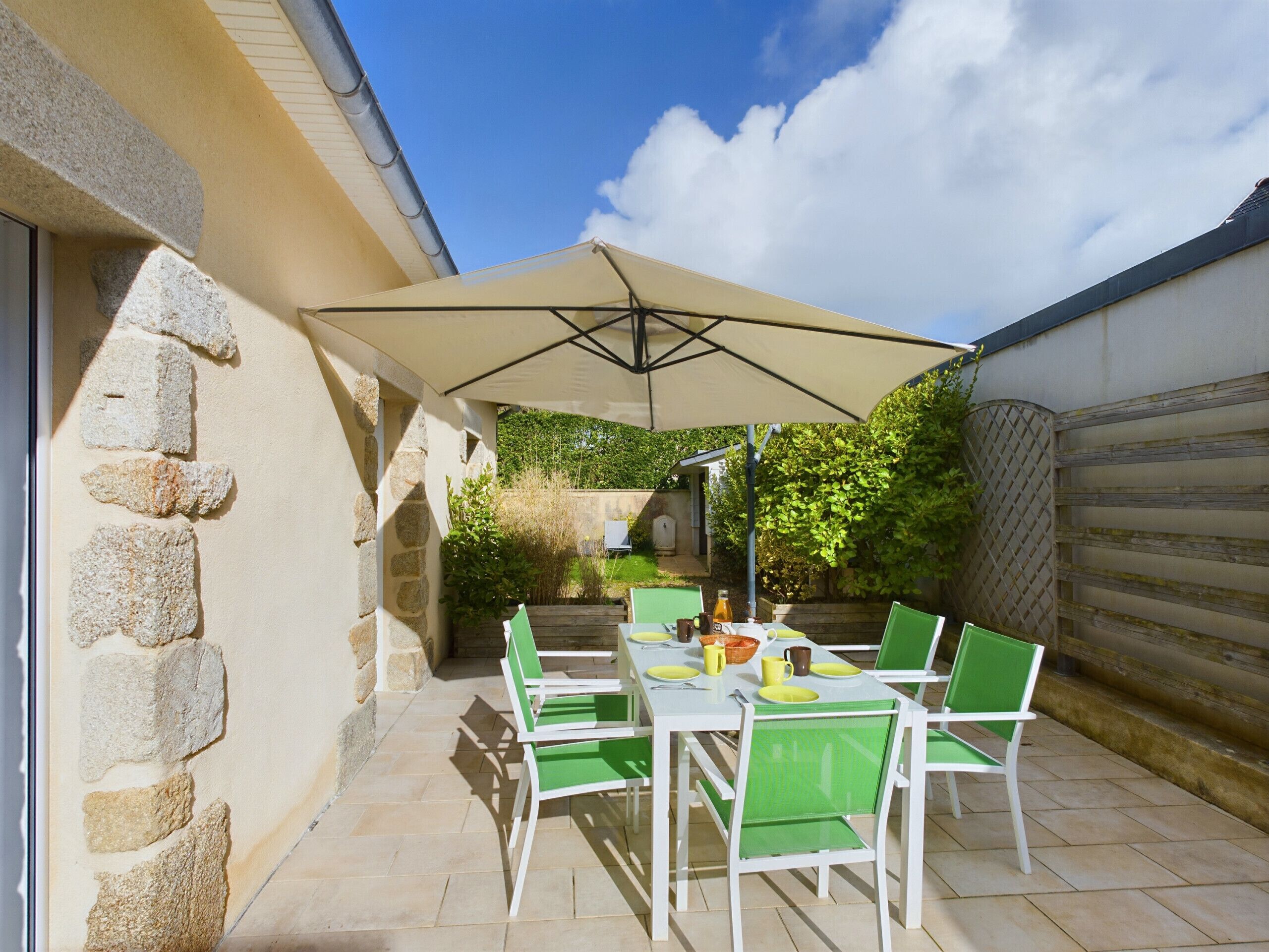Une terrasse extérieure avec une table et des chaises, un grand parasol et un mur en pierre.