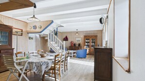 A spacious dining area with a wooden table and chairs, a staircase leading to another level, and a bookshelf in the background.