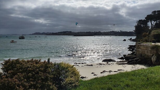 A coastal scene with a beach, rocky shoreline, and boats in the water.