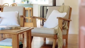 Una habitación acogedora con dos sillas de madera, cada una con cojín y manta. Una mesita con libros está frente a las sillas.
