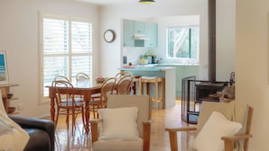 Amplia sala de estar con una mesa de comedor, sillas y un sofá. Se ve una cocina en el fondo, con armarios azul claro y una chimenea.