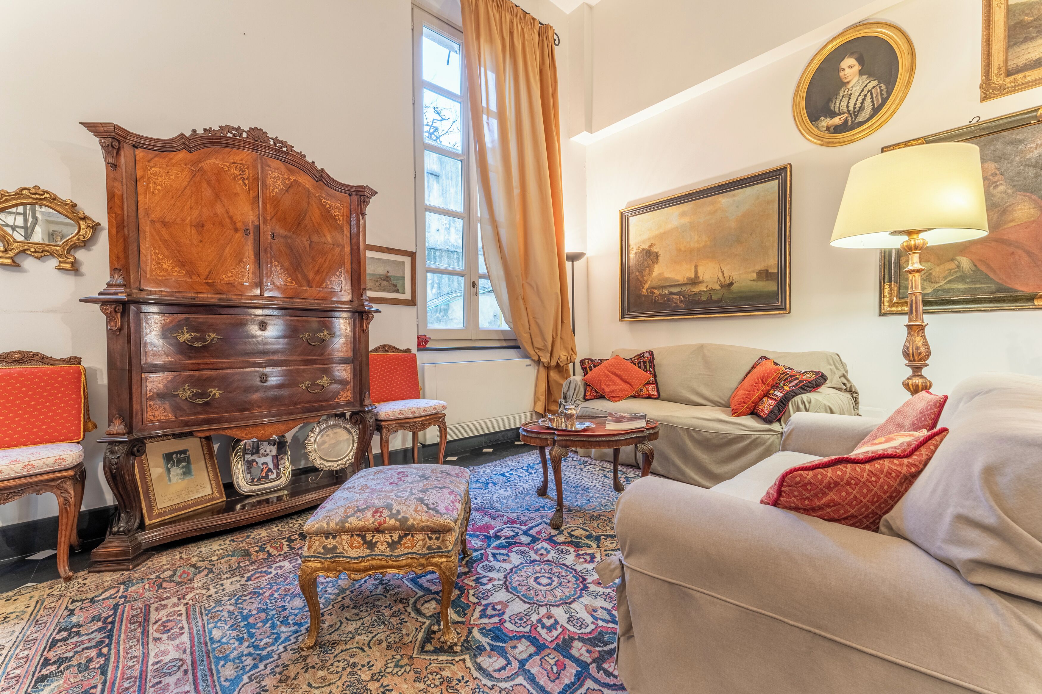 A traditional room with a wooden cabinet, a sofa, a patterned rug, and a painting on the wall.