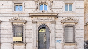 A historic building facade with a central arched entrance, flanked by two windows with metal grilles, and a plaque indicating it is the Deutsche Bank. - Portello Apartment By Geco Vacation Rentals (Genoa)