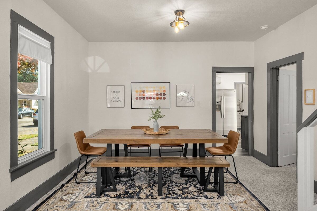 Uma sala de jantar com mesa e cadeiras de madeira, um tapete e quadros nas paredes.