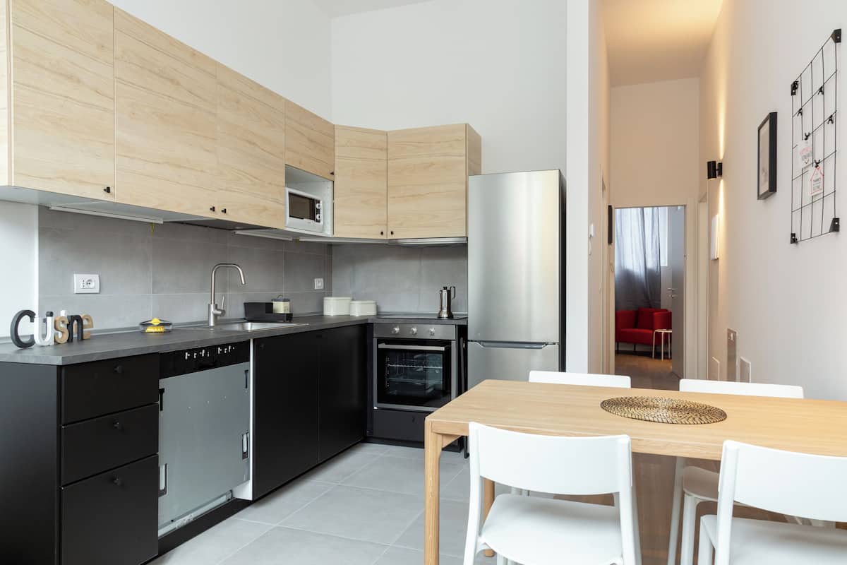 A modern kitchen with black and wooden cabinets, a stainless steel refrigerator, and a wooden dining table with white chairs.