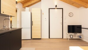 A modern kitchen with wooden cabinets, a white refrigerator, a wooden door, and a television on a white stand. - JOIVY Contemporary Apartments (Milan)