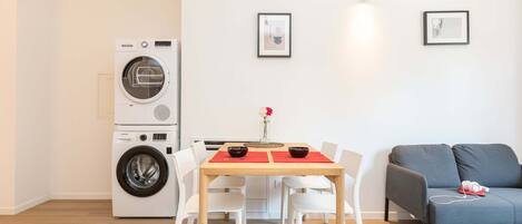 Un espacio habitable compacto con lavadora, una mesa de comedor con sillas y un sofá.