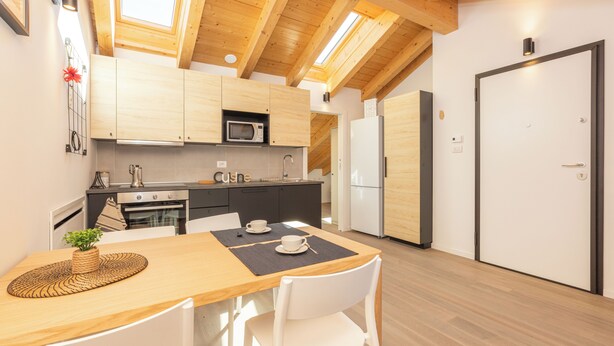 A modern kitchen with wooden cabinets, a microwave, a sink, and a dining area with a table and chairs. - JOIVY Contemporary Apartments (Milan)