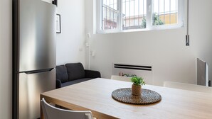 A modern kitchen with a stainless steel refrigerator, a dining table with a woven placemat, and a window with a view of buildings. - JOIVY Contemporary Apartments (Milan)