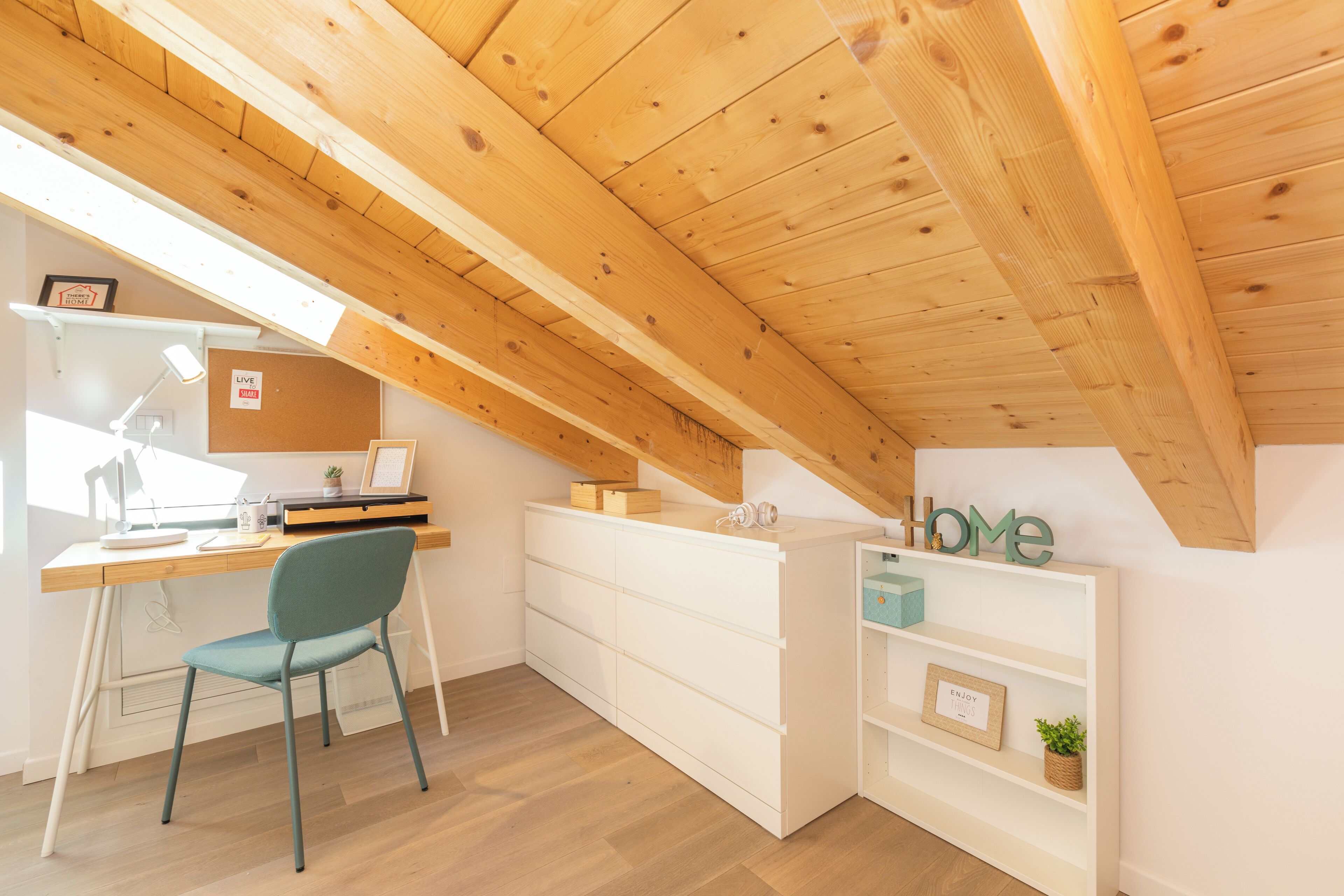 Un dormitori tipus loft modern amb un sostre inclinat, bigues de fusta, un escriptori amb una cadira, una biblioteca i una petita planta.