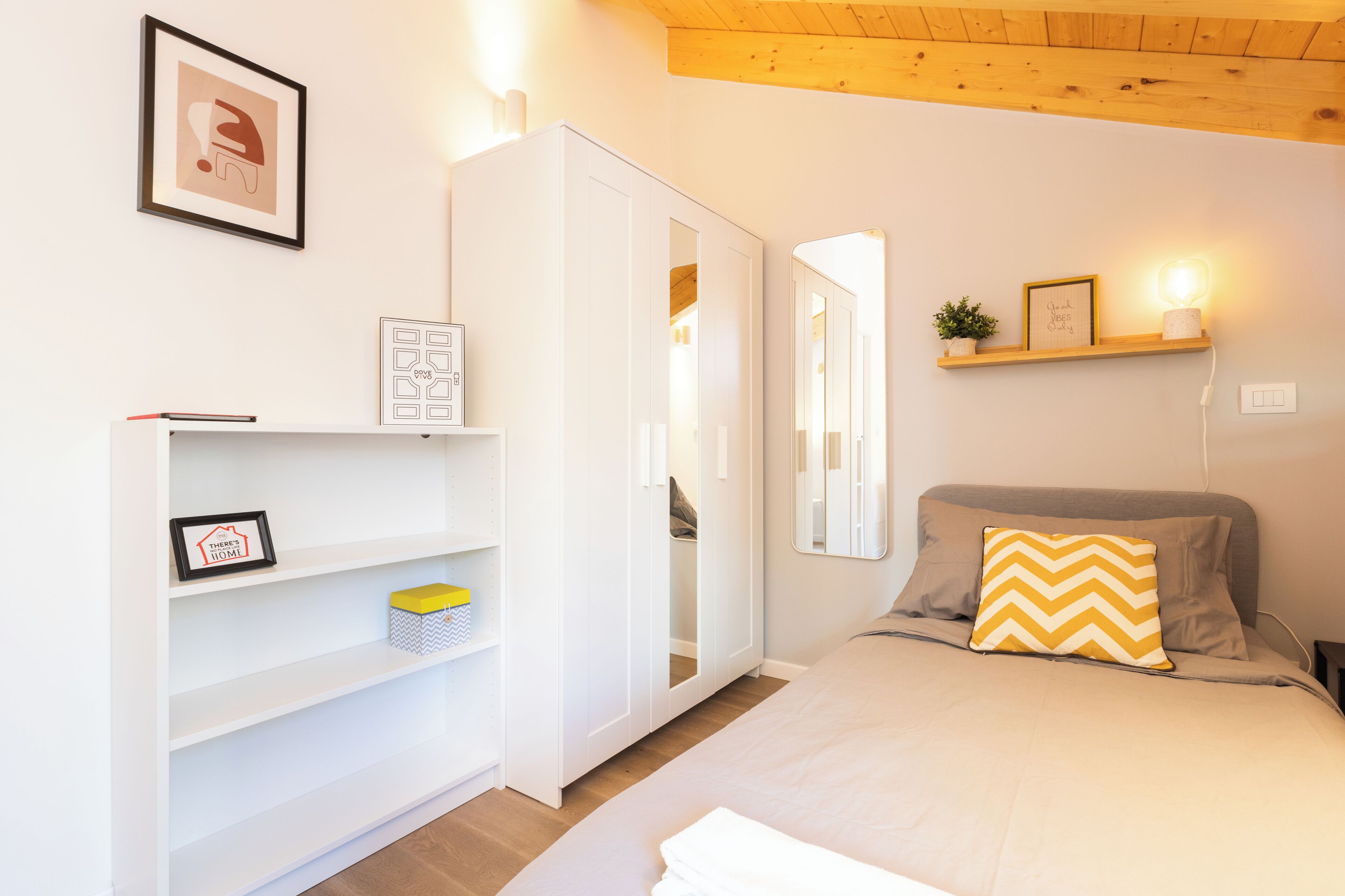 Una camera da letto con un letto, un armadio, una mensola con quadri incorniciati e un comodino con una lampada.