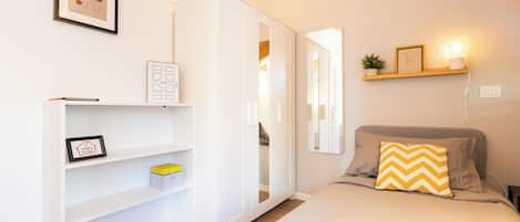 Una camera da letto con un letto, un armadio, una mensola con quadri incorniciati e un comodino con una lampada.