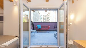 An open sliding door leading to an outdoor balcony with a red bench and a table. - JOIVY Contemporary Apartments (Milan)