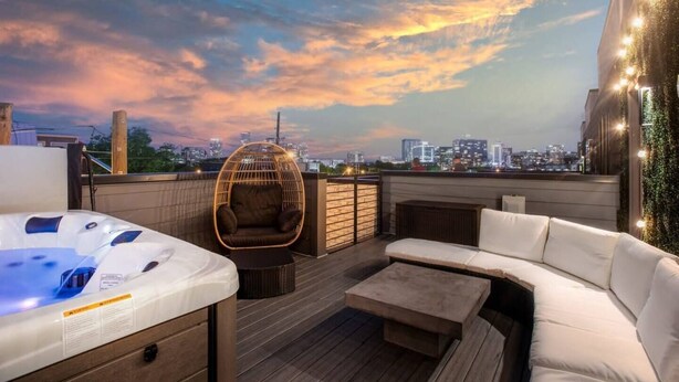 A rooftop terrace with a hot tub, a wicker chair, and a sofa. - Electric House | Walk to Gulch • Rooftop Hot Tub (Nashville)