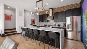 A modern kitchen with a central island, dark cabinets, stainless steel appliances, and a patterned backsplash. - Electric House | Walk to Gulch • Rooftop Hot Tub (Nashville)