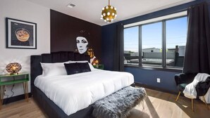 A modern bedroom with a large bed, a view of the sky through a window, and a unique wall art piece. - Electric House | Walk to Gulch • Rooftop Hot Tub (Nashville)